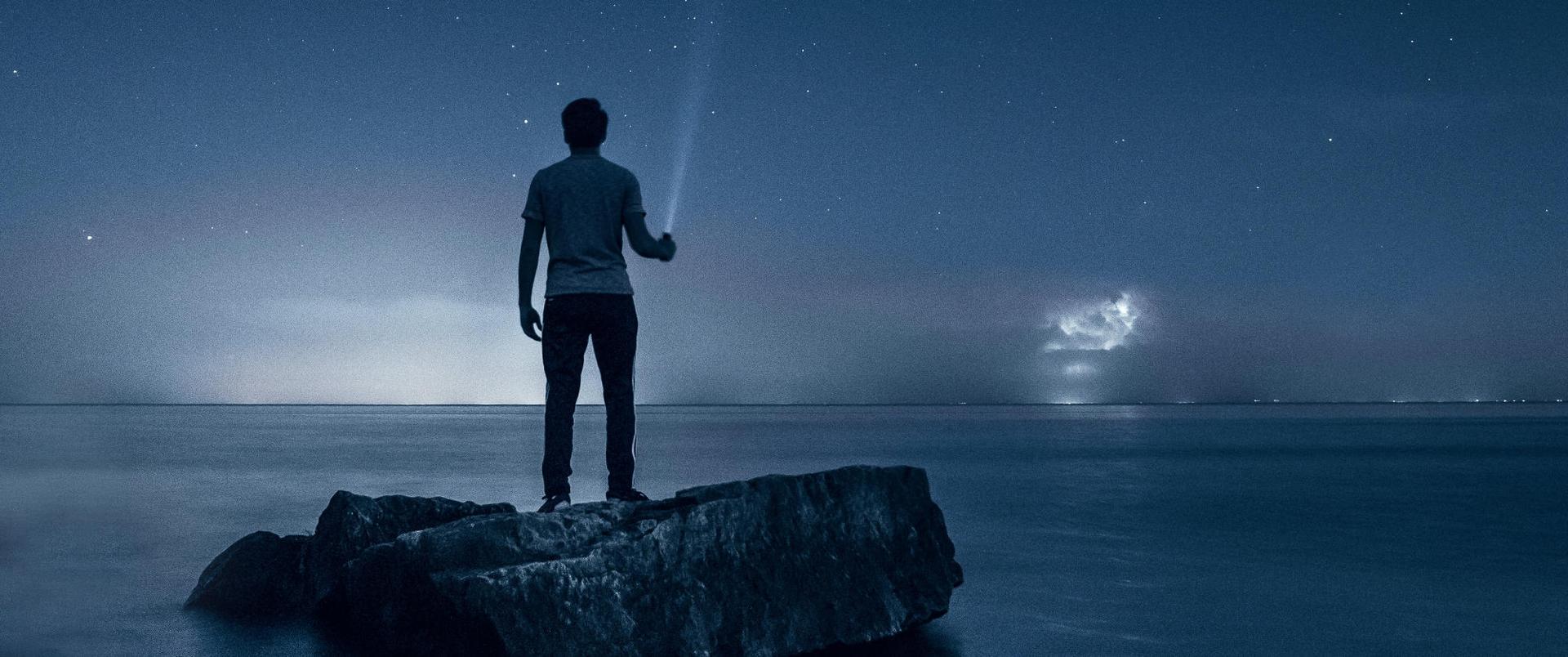Person shining an torch at night in front of a body of water Person shining an torch at night in front of a body of water